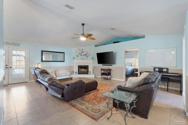 tiled living room featuring french doors, ceiling fan, lofted ceiling, and a tiled fireplace