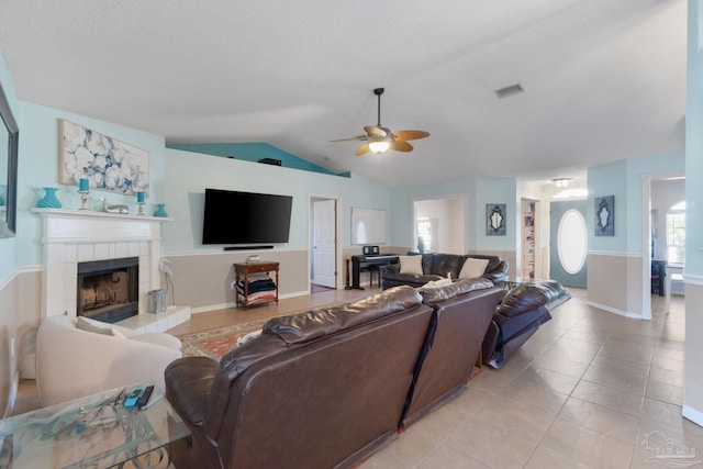 tiled living room featuring a tile fireplace, a textured ceiling, vaulted ceiling, and ceiling fan