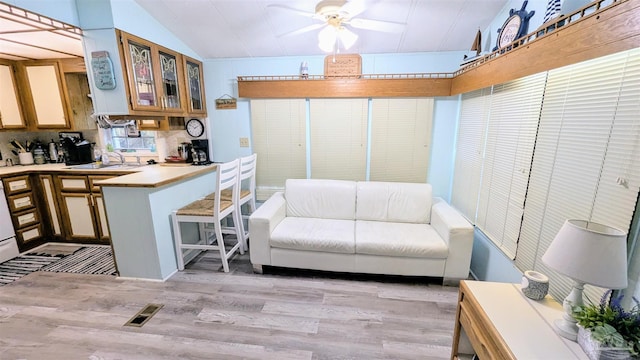 living room featuring sink, ceiling fan, light hardwood / wood-style flooring, and vaulted ceiling