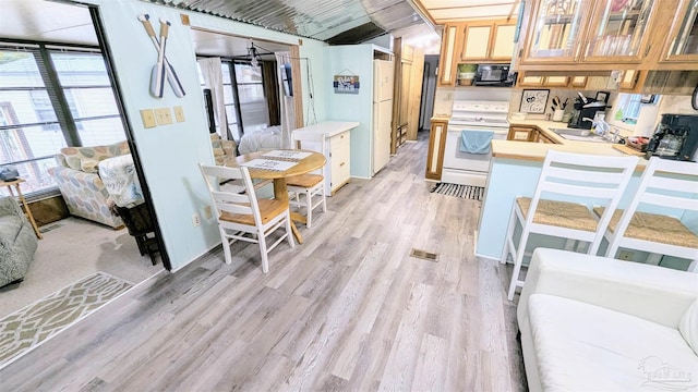 kitchen featuring kitchen peninsula, light hardwood / wood-style flooring, white electric range, black microwave, and sink