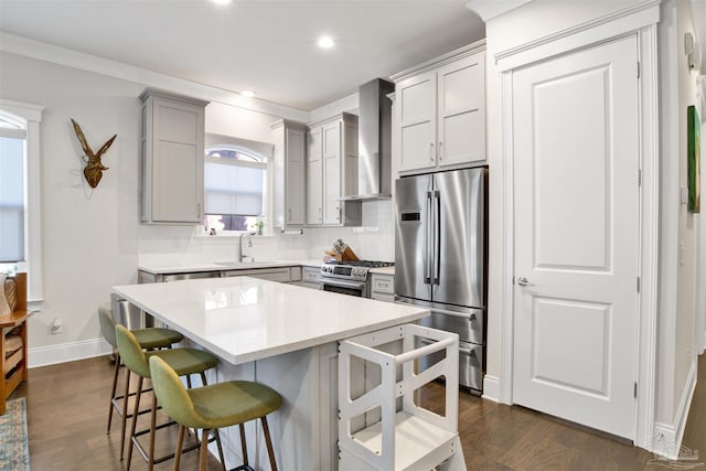 kitchen with dark wood-style floors, a breakfast bar, a sink, stainless steel appliances, and wall chimney range hood