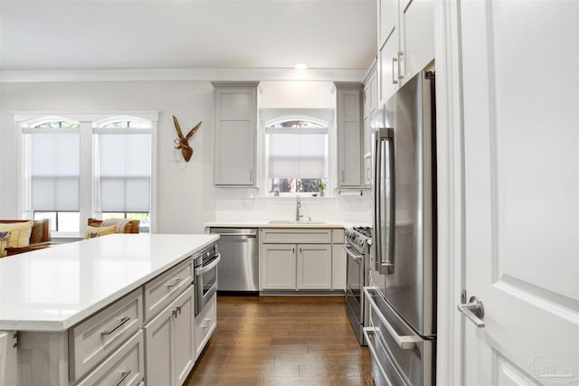 kitchen with a sink, a kitchen island, dark wood-style floors, stainless steel appliances, and crown molding