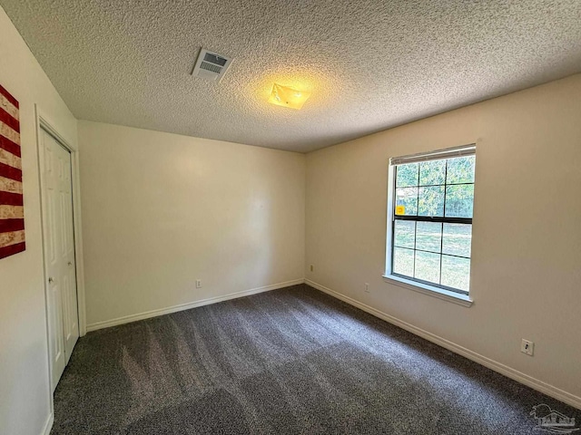 spare room featuring a textured ceiling, baseboards, visible vents, and dark carpet