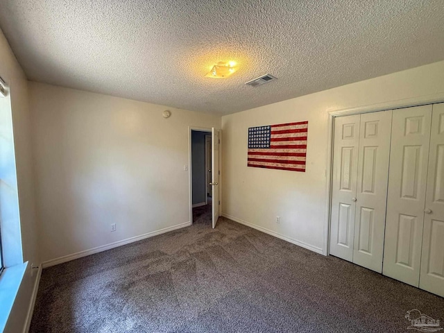 unfurnished bedroom featuring a closet, a textured ceiling, carpet, baseboards, and visible vents