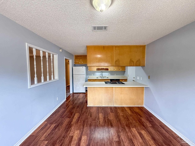 kitchen featuring a peninsula, a sink, freestanding refrigerator, brown cabinetry, and visible vents