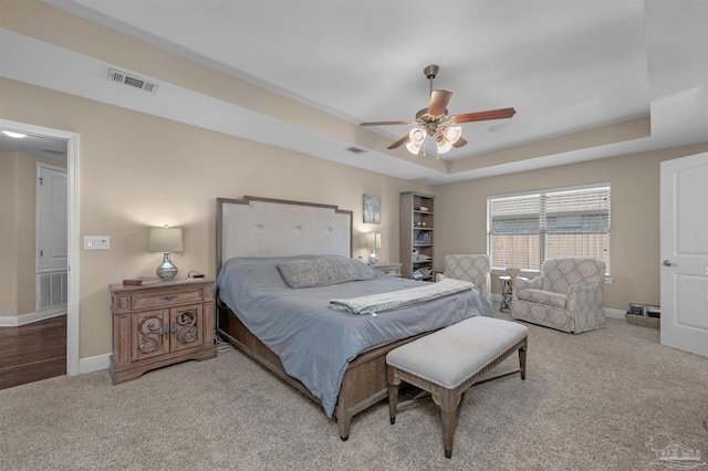 carpeted bedroom with ceiling fan and a raised ceiling