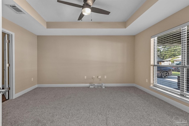 empty room featuring carpet floors, a tray ceiling, and ceiling fan