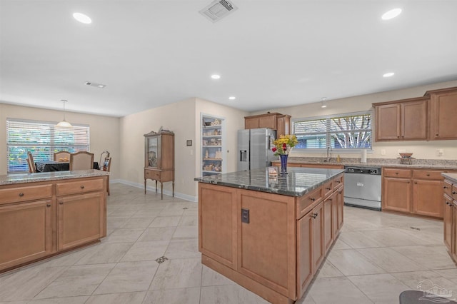 kitchen with appliances with stainless steel finishes, dark stone countertops, plenty of natural light, and a kitchen island