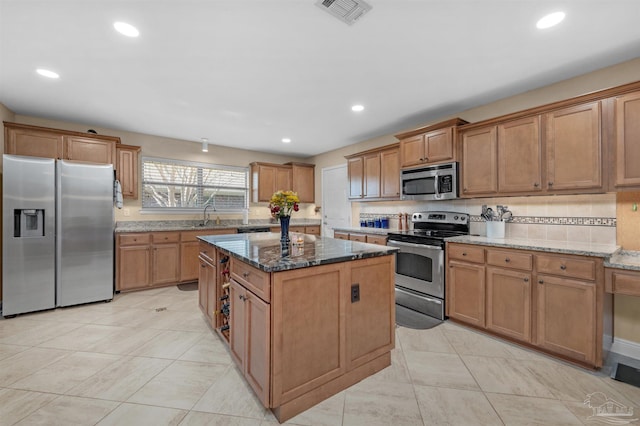 kitchen with dark stone countertops, a center island, stainless steel appliances, and sink