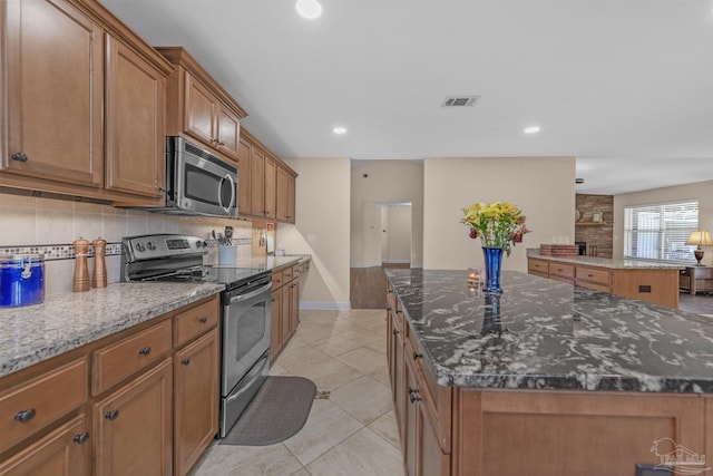 kitchen featuring light tile patterned floors, appliances with stainless steel finishes, dark stone counters, a fireplace, and a center island