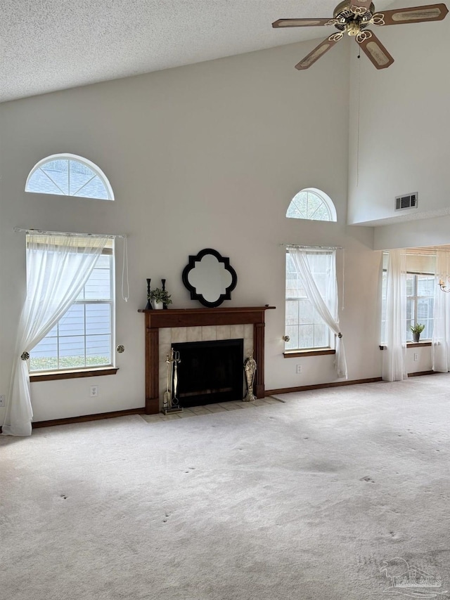 unfurnished living room featuring ceiling fan, a tile fireplace, carpet, and a textured ceiling