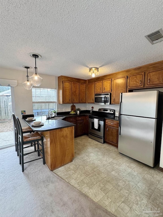 kitchen with appliances with stainless steel finishes, sink, a kitchen breakfast bar, hanging light fixtures, and kitchen peninsula