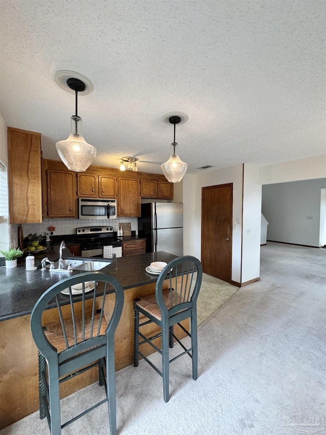 kitchen featuring sink, kitchen peninsula, pendant lighting, light colored carpet, and stainless steel appliances