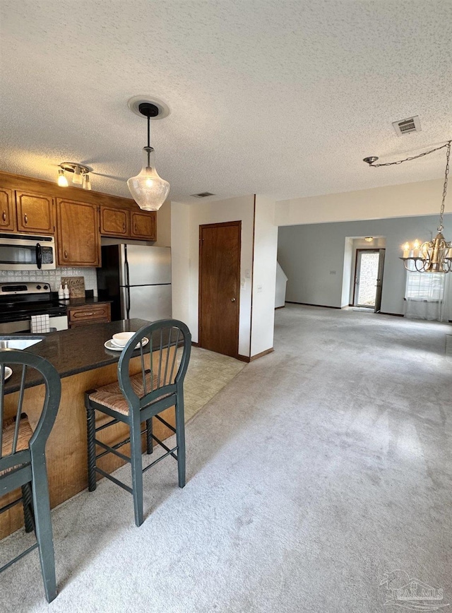 kitchen with light colored carpet, stainless steel appliances, hanging light fixtures, and a notable chandelier