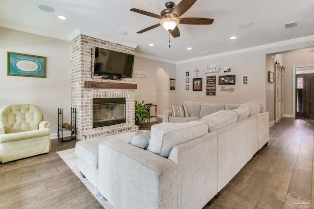 living room featuring hardwood / wood-style floors, ornamental molding, a brick fireplace, and ceiling fan