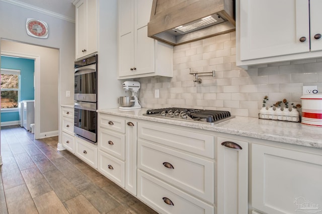 kitchen with premium range hood, white cabinetry, decorative backsplash, stainless steel appliances, and light stone countertops