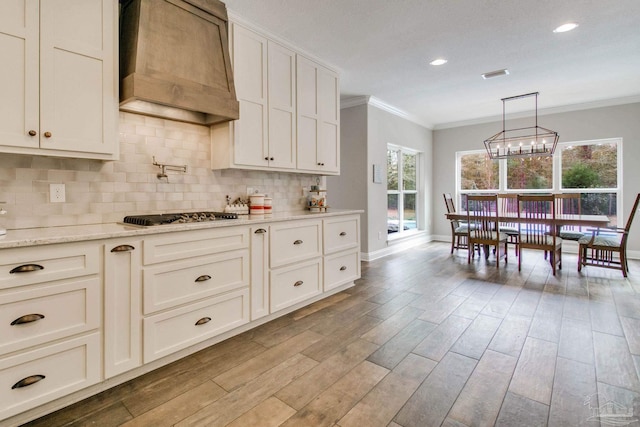 kitchen featuring premium range hood, stainless steel gas cooktop, white cabinetry, light stone countertops, and backsplash