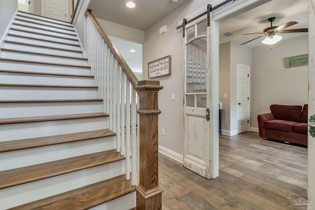 staircase featuring hardwood / wood-style flooring, ceiling fan, and a barn door