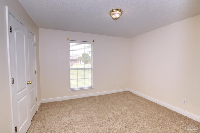 spare room with a textured ceiling, baseboards, and light carpet