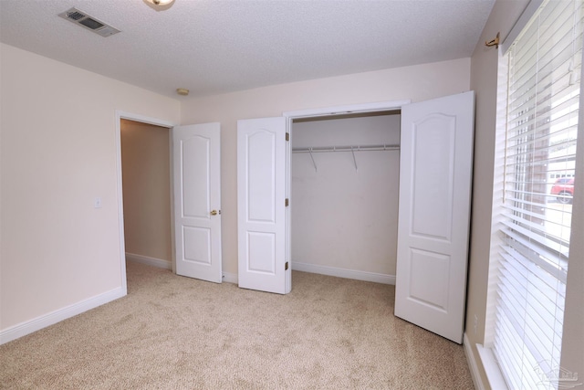 unfurnished bedroom with a textured ceiling, carpet, baseboards, visible vents, and a closet
