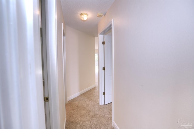 corridor with baseboards and light colored carpet