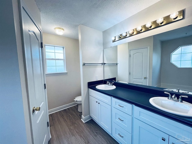 full bathroom with a sink, double vanity, toilet, and wood finished floors