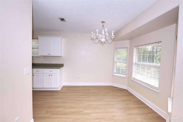 unfurnished dining area featuring an inviting chandelier, a textured ceiling, light wood finished floors, and baseboards