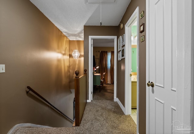 corridor featuring light colored carpet, attic access, a textured ceiling, an upstairs landing, and baseboards