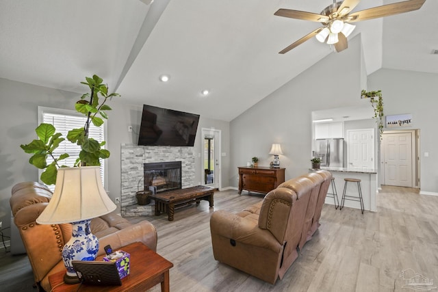 living area featuring a stone fireplace, light wood-style flooring, baseboards, and a ceiling fan