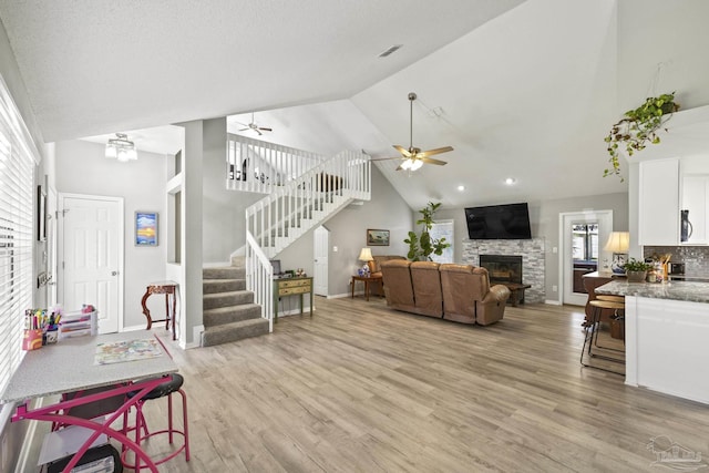 living room with stairs, a ceiling fan, light wood-type flooring, and high vaulted ceiling