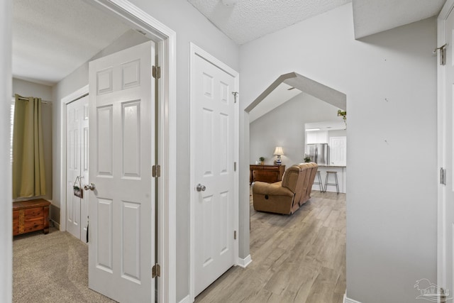 corridor with a textured ceiling and light wood-style flooring