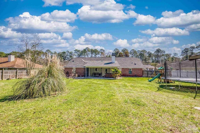 back of property featuring a lawn, a trampoline, a fenced backyard, a playground, and a patio area