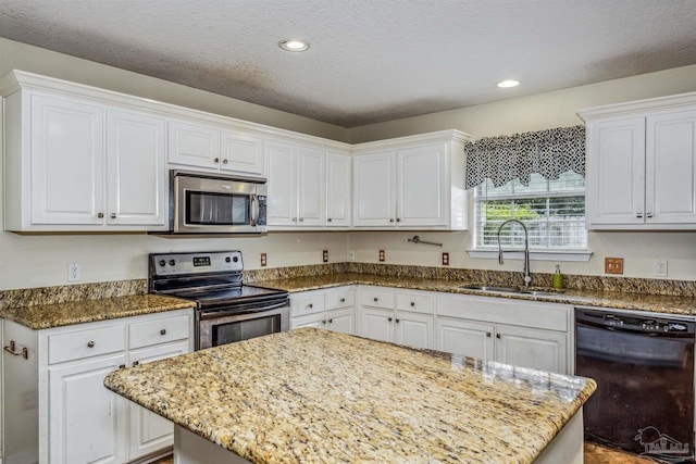 kitchen with stainless steel appliances, light stone counters, a sink, and white cabinetry