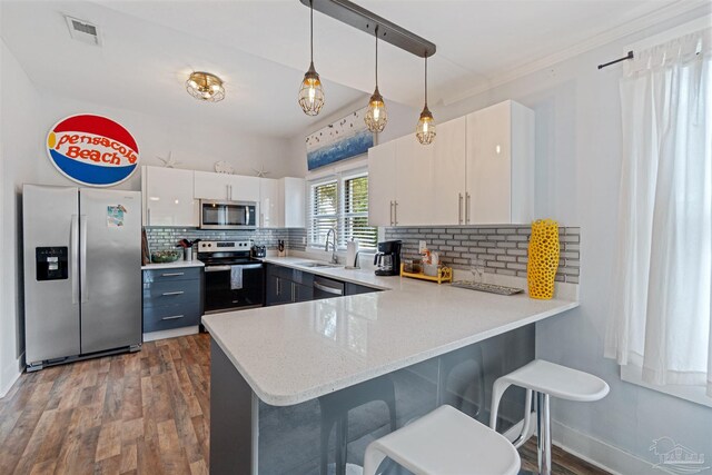 kitchen with appliances with stainless steel finishes, decorative light fixtures, dark hardwood / wood-style floors, tasteful backsplash, and kitchen peninsula