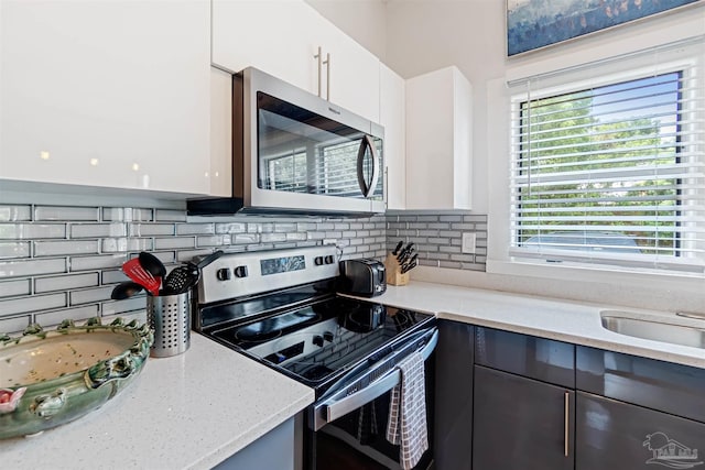 kitchen featuring modern cabinets, appliances with stainless steel finishes, light stone countertops, white cabinetry, and backsplash