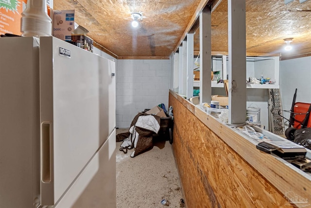 interior space featuring freestanding refrigerator and concrete block wall