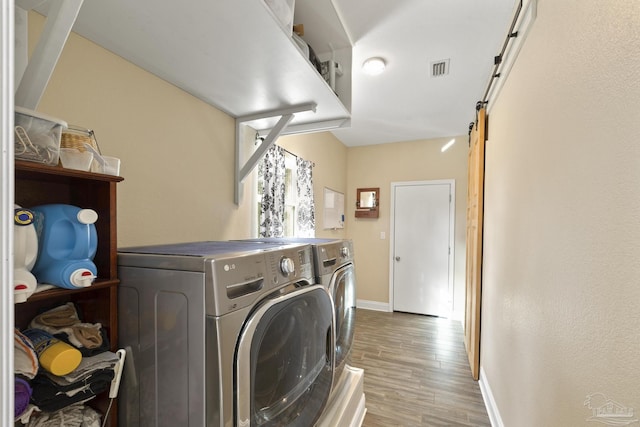 laundry room featuring light hardwood / wood-style flooring, independent washer and dryer, and a barn door