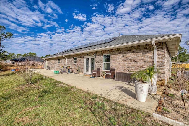 rear view of property featuring french doors, a yard, a patio area, and solar panels