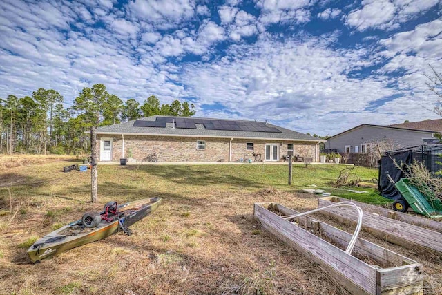 rear view of property with a lawn and solar panels