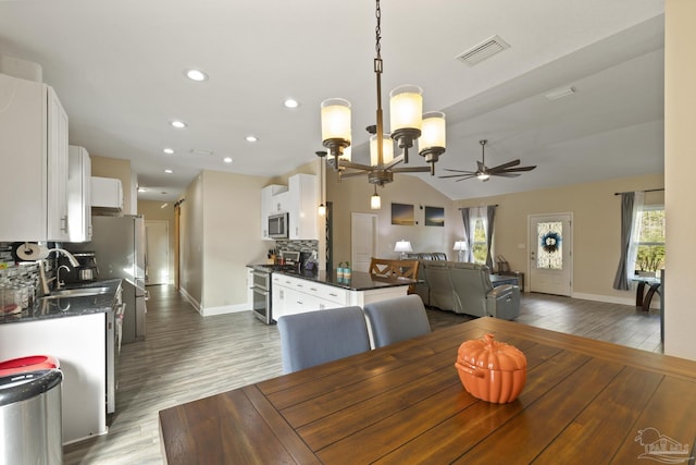 dining space with dark hardwood / wood-style flooring, sink, ceiling fan with notable chandelier, and vaulted ceiling