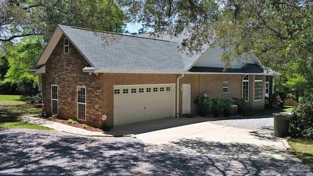 view of side of home with concrete driveway, stone siding, an attached garage, and roof with shingles