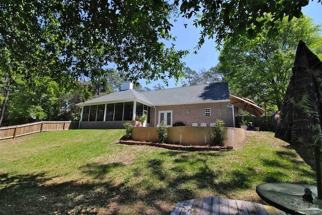 back of house with a fenced backyard, french doors, a chimney, a sunroom, and a lawn