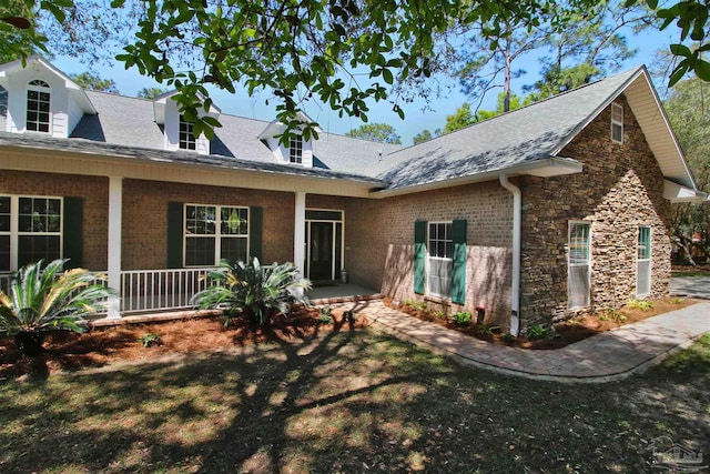 view of front of home with covered porch, brick siding, a shingled roof, and stone siding