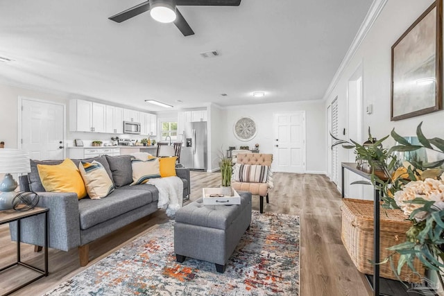 living room featuring ceiling fan, ornamental molding, and light wood-type flooring