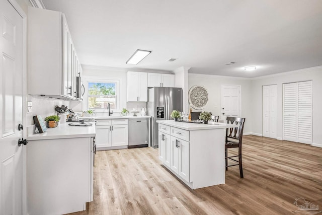 kitchen featuring a kitchen breakfast bar, light wood-type flooring, stainless steel appliances, a center island, and white cabinetry