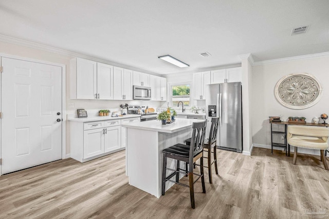 kitchen featuring a center island, crown molding, appliances with stainless steel finishes, white cabinetry, and a breakfast bar area