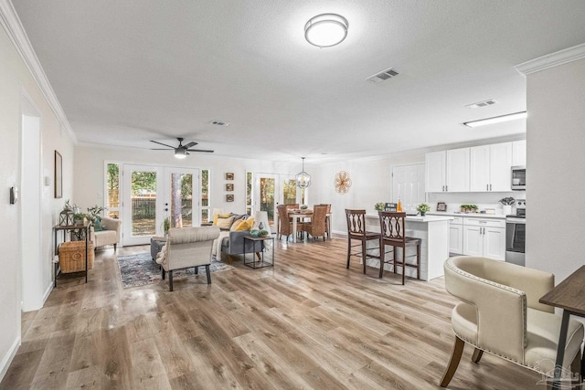 living room featuring french doors, ceiling fan with notable chandelier, ornamental molding, light wood-type flooring, and a textured ceiling