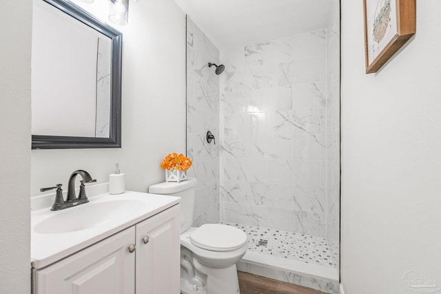 bathroom with a tile shower, hardwood / wood-style floors, vanity, and toilet