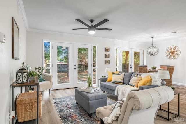 living room with french doors, ornamental molding, ceiling fan with notable chandelier, and light hardwood / wood-style flooring