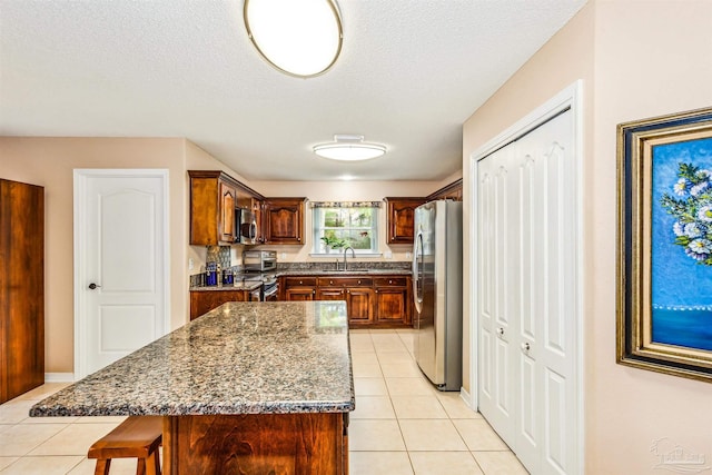 kitchen featuring stainless steel appliances, a center island, sink, light tile patterned flooring, and a breakfast bar